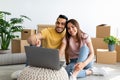 Cheerful diverse couple with laptop searching for household goods for their new home online, using pc on moving day Royalty Free Stock Photo