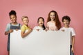 Cheerful diverse schoolkids holding blank banner with space for design over pink background