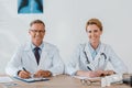 cheerful doctors looking at camera and smiling while sitting near table.