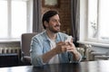 Cheerful dreamy millennial cellphone user man holding mobile phone