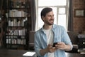 Cheerful dreamy millennial smartphone user man holding cell