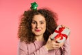 Cheerful ecxited woman with curly hair smiling and holding gift box pink studio