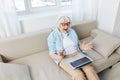 a cheerful elderly business lady is sitting on the couch working on a laptop from home and enthusiastically