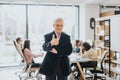 A cheerful elderly businessman stands smiling, giving a thumbs-up with a team of professionals working in the background Royalty Free Stock Photo