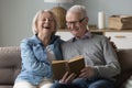 Cheerful elderly couple of pensioners reading funny classical novel together