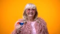 Cheerful elderly lady in funny pink outfit drinking blue cocktail, age positive