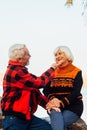 Cheerful elderly people a woman and a man are sitting on the stones and hugging on the lake, against the background of the bridge Royalty Free Stock Photo