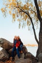 Cheerful elderly people a woman and a man are sitting on the stones and hugging on the lake, against the background of the bridge Royalty Free Stock Photo