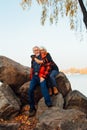 Cheerful elderly people a woman and a man are sitting on the stones and hugging on the lake, against the background of the bridge Royalty Free Stock Photo