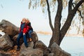 Cheerful elderly people a woman and a man are sitting on the stones and hugging on the lake, against the background of the bridge Royalty Free Stock Photo
