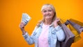 Cheerful elderly woman holding shopping bags and dollar cash, consumerism Royalty Free Stock Photo