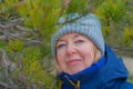 Cheerful elderly woman smiling outdoors. Cold windy weather. Close up face. Pine tree background Royalty Free Stock Photo