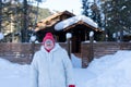 Cheerful elderly woman stands and smiles happily in front of a rustic wooden house among the snowdrifts in the forest Royalty Free Stock Photo