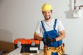 Cheerful electrician technician in uniform, hard hat and protective gloves smiling at camera while posing indoors Royalty Free Stock Photo