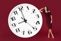 Cheerful elegant young modern business woman in maroon dress lean against giant white clock over red background. Royalty Free Stock Photo