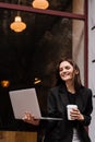 Cheerful emotional young woman is working online on laptop and sitting on summer terrace in cafe. Happy excited girl Royalty Free Stock Photo