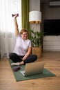 Cheerful energetic senior woman with dumbbells sitting on floor on sports mat and watching online workout Royalty Free Stock Photo