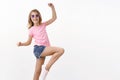 Cheerful energized and charismatic little blond girl in summer sunglasses, pink t-shirt jumping, lift leg posing