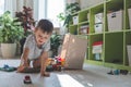 A cheerful European boy plays with cars on the carpet in his room.