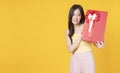 Cheerful excited asian woman holding red gift box with ribbon in own hand while standing over isolated blue background. Surprise Royalty Free Stock Photo