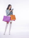 Cheerful excited asian woman touching mobile phone screen carrying shopping bags full body standing on white background. Joyful Royalty Free Stock Photo