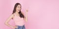 Cheerful excited asian woman use finger pointing to side with product or empty copy space standing over  pink background. Royalty Free Stock Photo