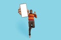 Cheerful Excited Black Male Jumping With Big Blank Mobile Phone In Hand