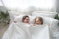 Cheerful excited Caucasian married couple lying in bed hiding bodies under white blanket