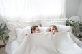 Cheerful excited Caucasian married couple lying in bed hiding bodies under white blanket