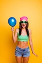 Cheerful excited hipster girl in pink hat holding balloon on yellow wall