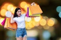 Excited young woman holding colorful shopping bags pointing fingers on bokeh light soft effect background. Happiness, Royalty Free Stock Photo