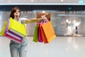 Excited young woman holding colorful shopping bags pointing fingers to shopping malls background. Happiness, consumerism Royalty Free Stock Photo