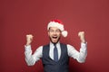 Cheerful exited businessman in Chtistmas hat smiling on red studio wall background
