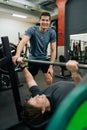 Cheerful experienced fitness instructor helping smiling beginner sportsman doing barbell bench press exercise during Royalty Free Stock Photo