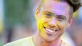 Cheerful face of young handsome man in coloured powder smiling to camera, fun