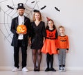 Cheerful family in carnival costumes celebrate Halloween near a gray wall with cobwebs and bats