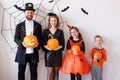 Cheerful family in carnival costumes celebrate Halloween near a gray wall with cobwebs and bats
