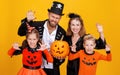 Cheerful family in carnival costumes does scary gesture and celebrate Halloween on colored yellow background