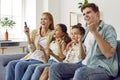 Cheerful family with children cheering together while watching TV at home in living room.