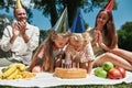 Cheerful family wearing party hats, celebrating birthday in the park on a summer day. Parents smiling and clapping hands Royalty Free Stock Photo