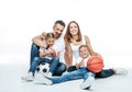 Cheerful family in white t-shirts and jeans sitting with soccer and basketball balls