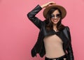 Cheerful fashion model adjusting hat and smiling, wearing sunglasses