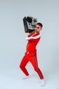 Cheerful fashionable man wearing a red sports suit dancing jumps with a retro tape recorder. interesting and fervent style of the