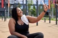 cheerful fat african woman is engaged in fitness sitting on mat taking selfie