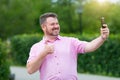 Cheerful fat man with a beard takes pictures of himself on a smartphone, selfie. Self-portrait in the park