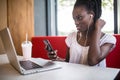 Cheerful female black model resting in coffee shop listening favorite music in headphones and chatting in networks. Beautiful dark