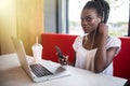 Cheerful female black model resting in coffee shop listening favorite music in headphones and chatting in networks. Beautiful dark