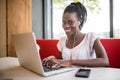 Cheerful female black model resting in coffee shop listening favorite music in headphones and chatting in networks. Beautiful dark