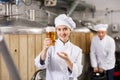 Cheerful female brewer holding out glass of craft beer