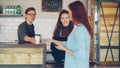 Cheerful female cashier is selling takeaway coffee to young woman and accepting payment while good-looking male barista Royalty Free Stock Photo